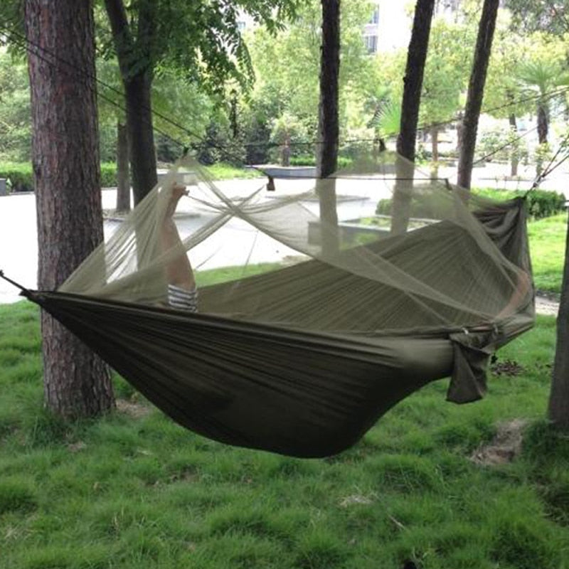 Camping hammock with mosquito net hanging between trees outdoors